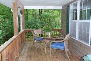 A wooden deck with a glass table and wicker chairs, surrounded by greenery. - 8 acres of privacy , stream and waterfall, Dupont, pets welcome. (Cedar Mountain)