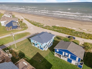 A coastal property with a large house featuring a blue exterior and a balcony, adjacent to a sandy beach and ocean. - Beachfront  Panoramic Views,  Covered Patio, Clean, 6 Miles from Town (galveston)