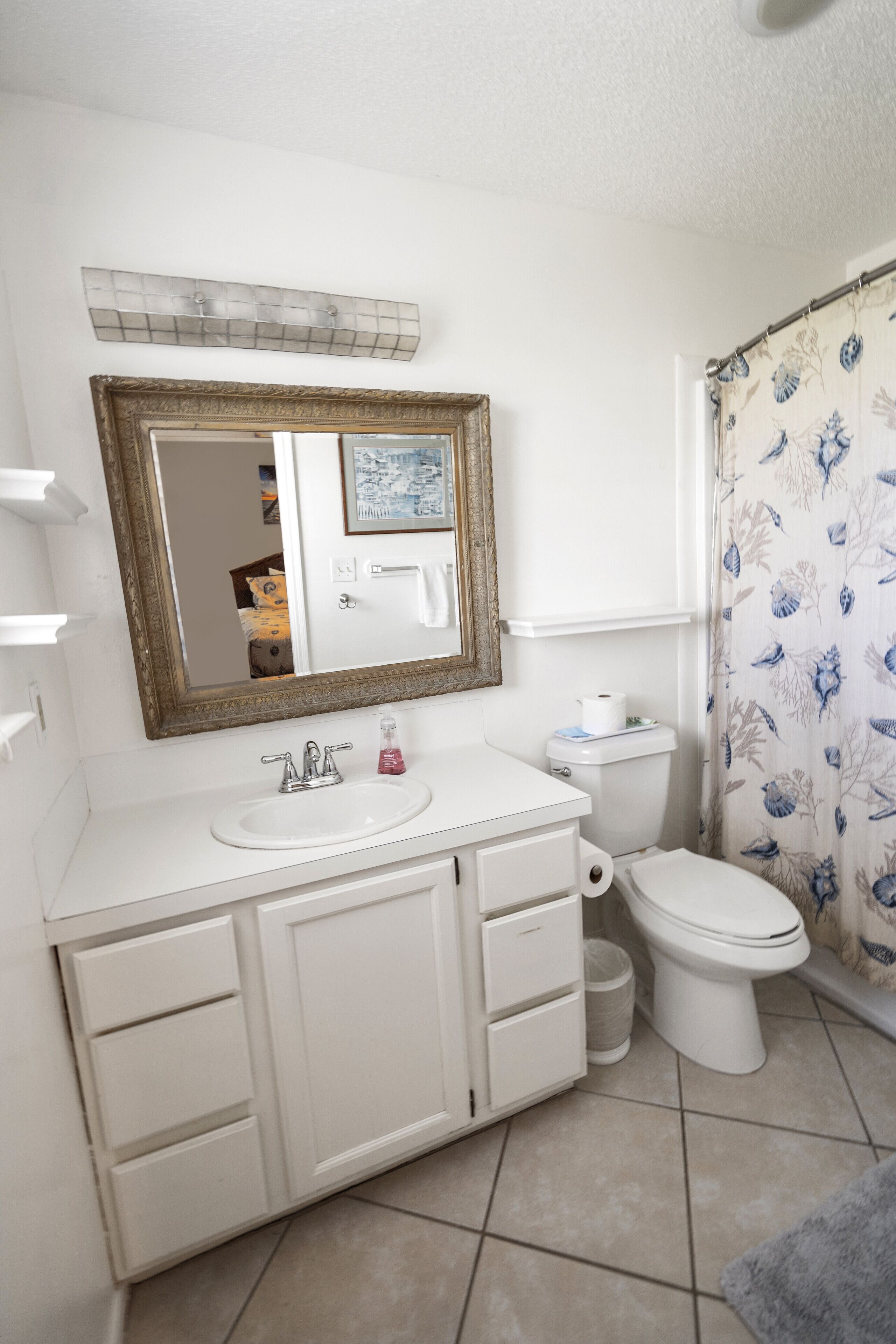 Une salle de bain avec un meuble-lavabo blanc, un miroir, des toilettes et un rideau de douche.