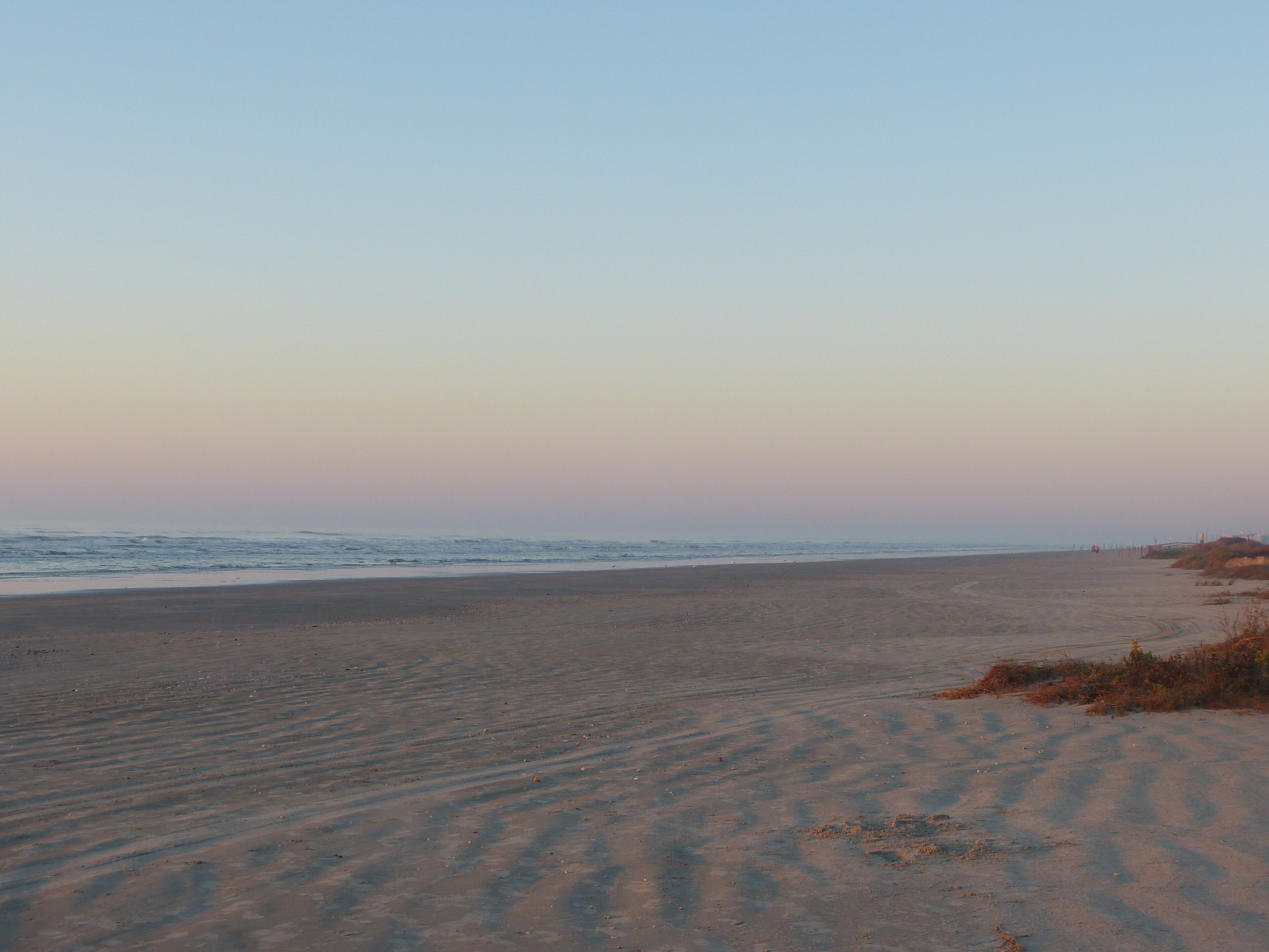 Een strand met een breed zandstrand en rustige golven.