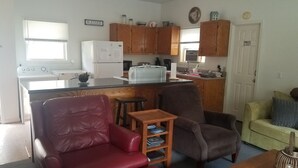 A compact living space with a kitchenette, a red leather chair, a wooden side table, and a green couch. - RIVERFRONT Cabin on Nantahala River, Minutes from NOC (Nantahala)