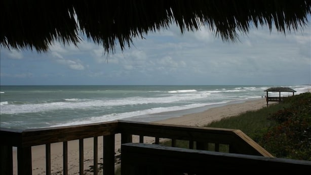 Vista a la playa con una terraza de madera y una estructura de techo de paja.