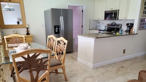Cocina moderna con refrigerador, microondas y cafetera. Hay una mesa de comedor con sillas y una pequeña isla con pileta.