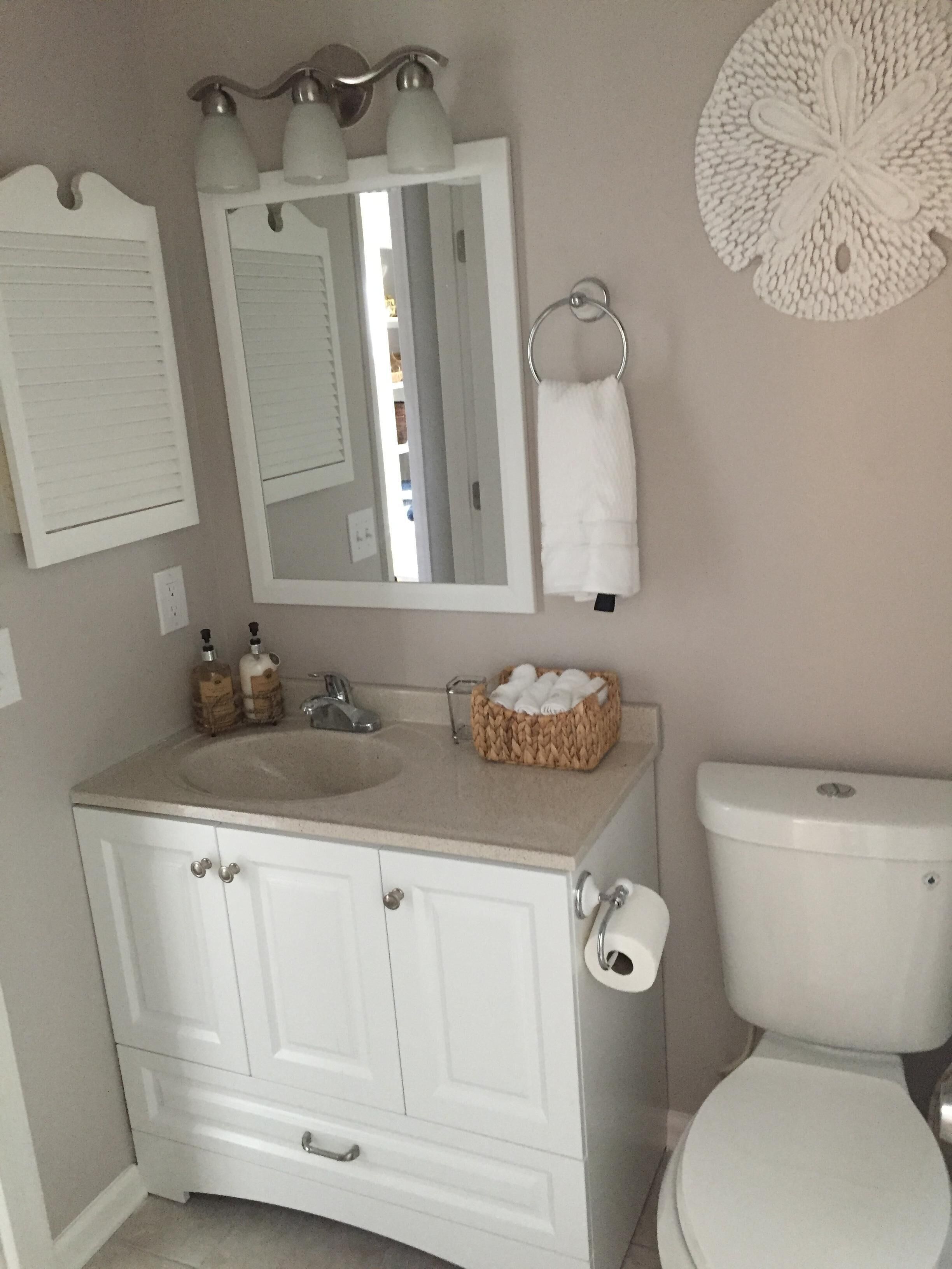 A bathroom with a white vanity, a sink, a mirror, a toilet, and a decorative wall piece.