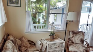 A room with a sofa, a chair, a small table with a plant, and a window with a view of a balcony and trees.