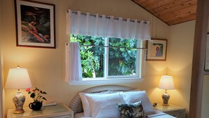 A bedroom with a bed, two bedside tables with lamps, a window with curtains, and a framed picture on the wall.