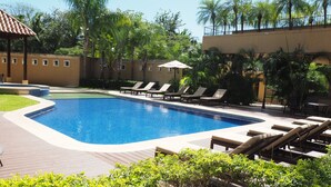 A swimming pool with lounge chairs and a small umbrella, surrounded by palm trees and greenery.