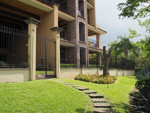 A multi-story building with a balcony, a well-maintained lawn, and a stone pathway leading to the entrance. - Crystal Sands, Luxury Living on the white Sands of Playa Langosta (Tamarindo)