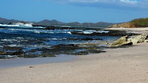 A beach with rocky shoreline, clear blue sky, and distant mountains.