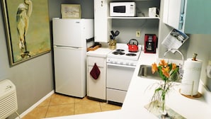Cocina compacta con electrodomésticos blancos, microondas, hervidor de agua y pileta. Hay un cuadro en la pared y un florero con flores en la encimera.