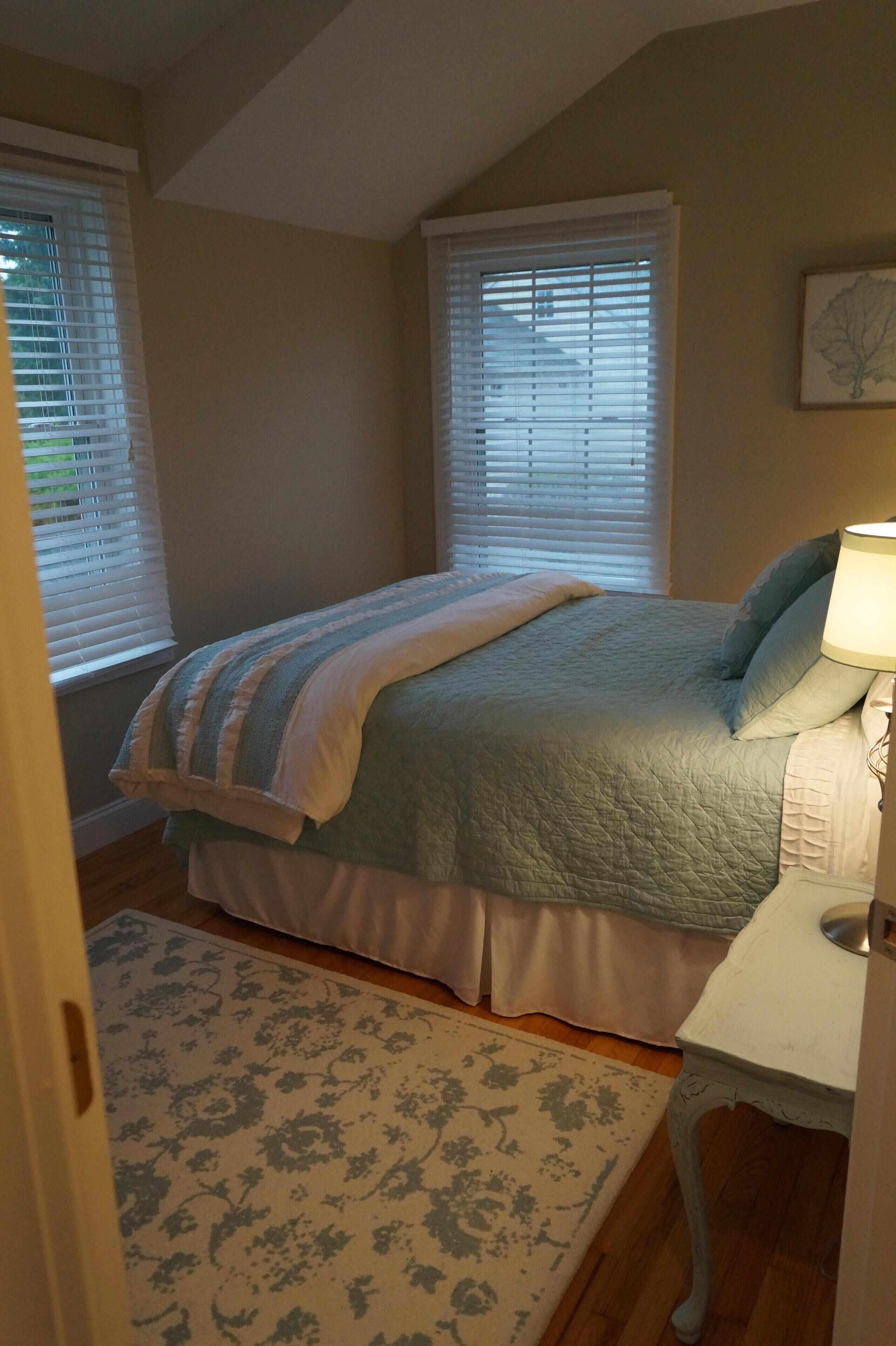 Une chambre à coucher avec un lit, une table de chevet, une lampe et une fenêtre avec des stores.
