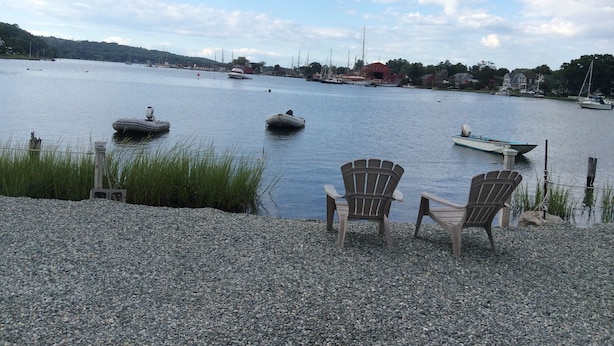 Una playa de guijarros con dos sillas de madera mirando un lago tranquilo con barcos.