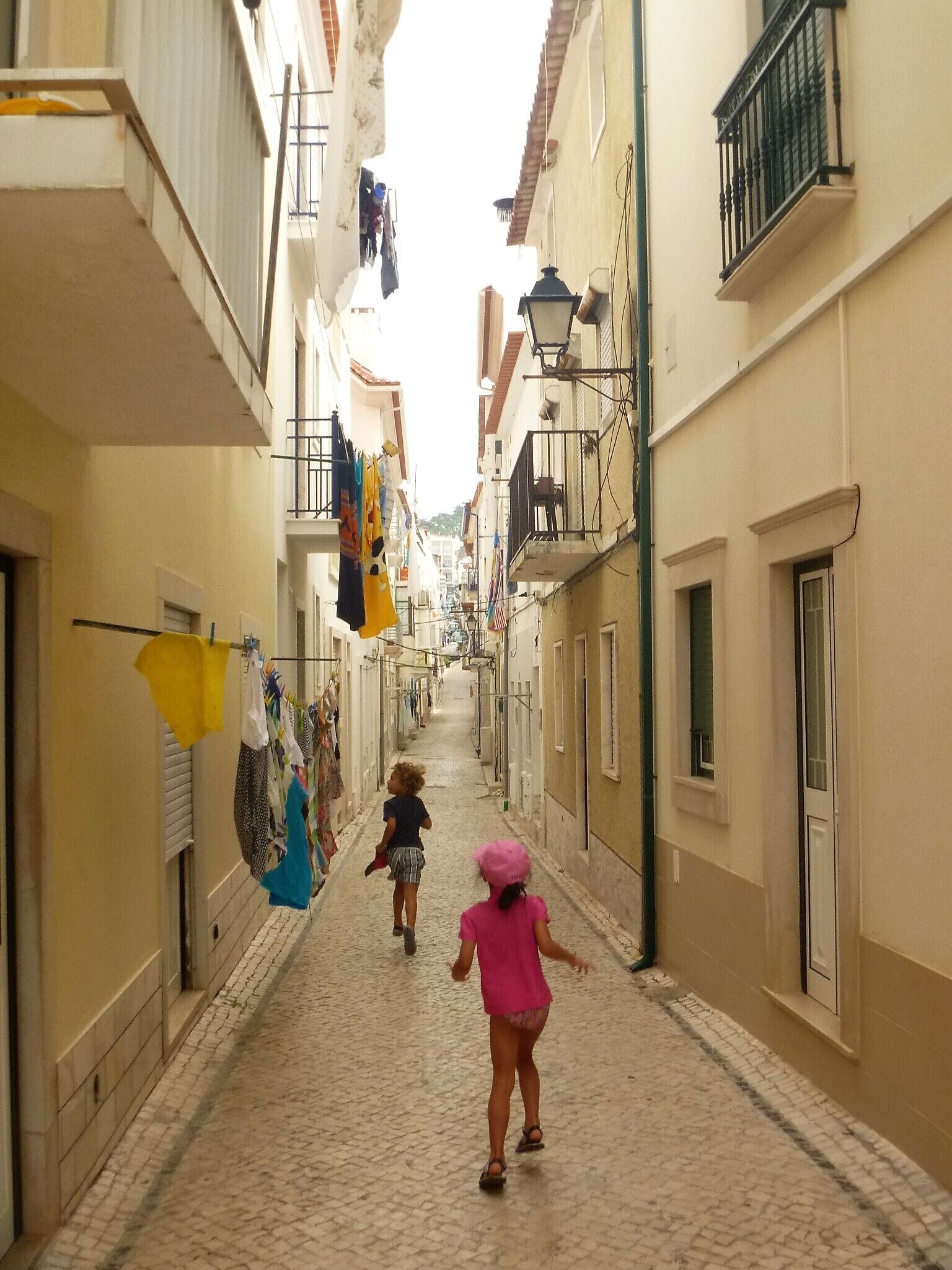 Un estrecho callejón empedrado flanqueado por edificios con balcones y ropa tendida.