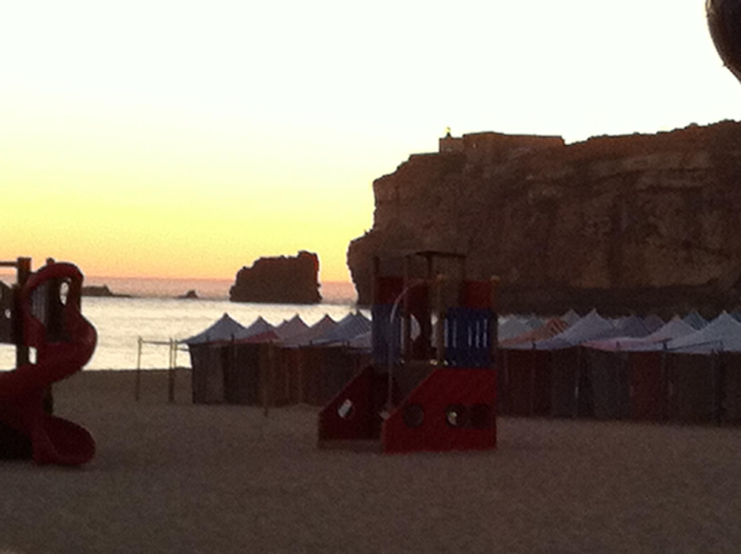 A beach with a large rock formation and a red play structure.