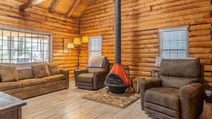 L’intérieur d’une cabane en rondins, avec une cheminée, deux canapés et deux fauteuils.