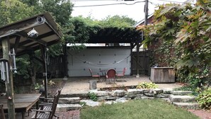 A backyard with a wooden deck, a hammock, a barbecue grill, and a stone wall. - iKlektik House Chicago (Chicago)