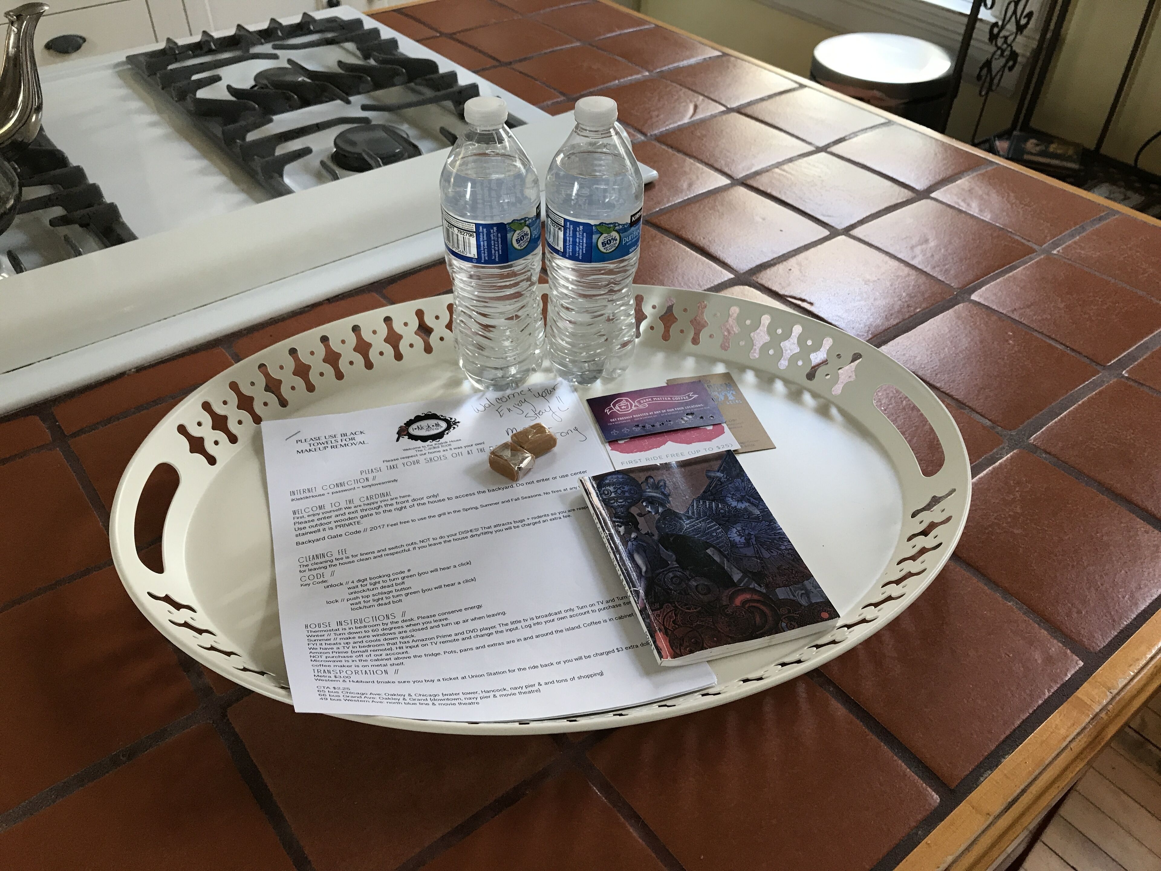Ein Tablett mit einem Zettel, zwei Wasserflaschen, einem kleinen Gegenstand und einer Karte auf einer gefliesten Tischplatte.
