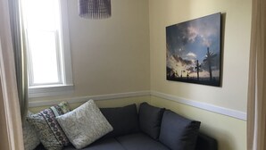 A corner room with a dark grey sofa, patterned pillows, a small wooden stool, and a painting of a sunset on the wall. - iKlektik House Chicago (Chicago)