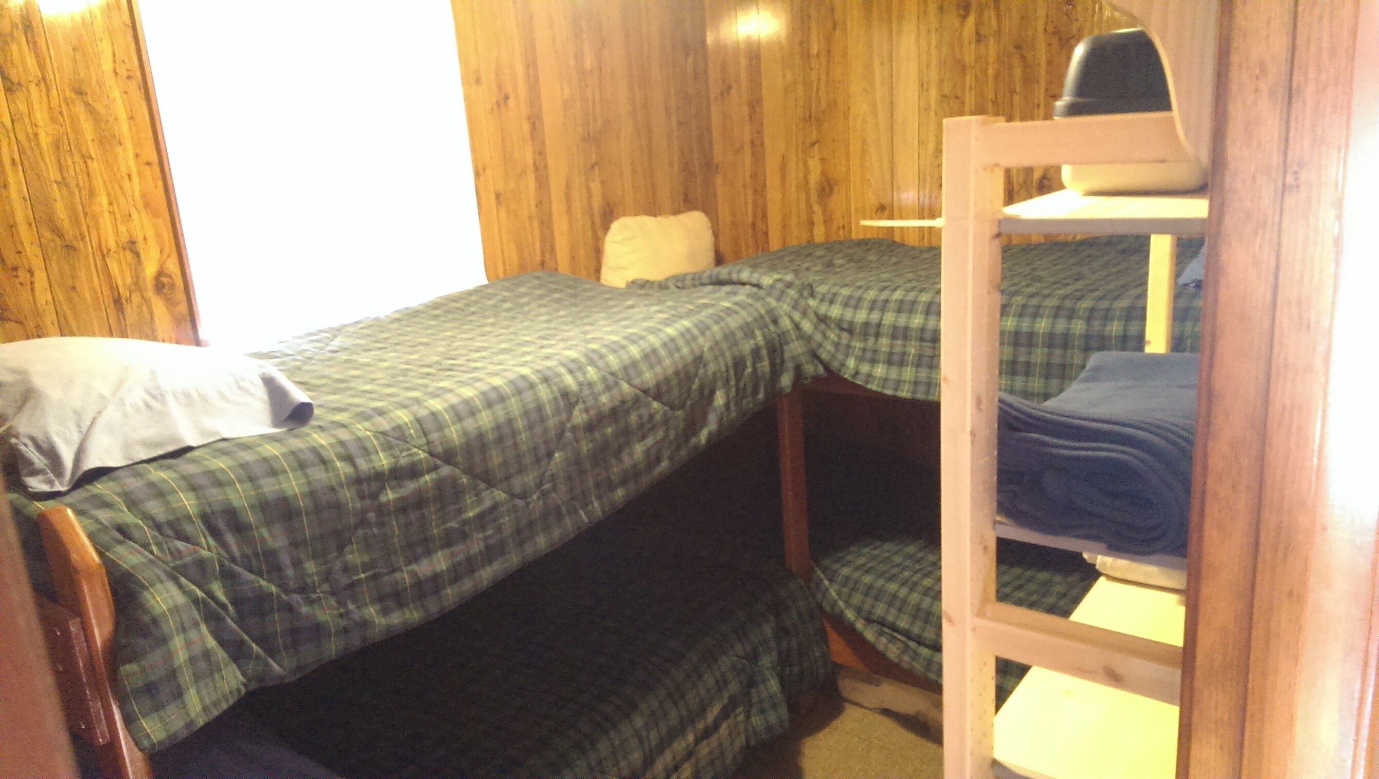 A small, compact room with two bunk beds and a single bed, wooden walls, and a simple, functional design.