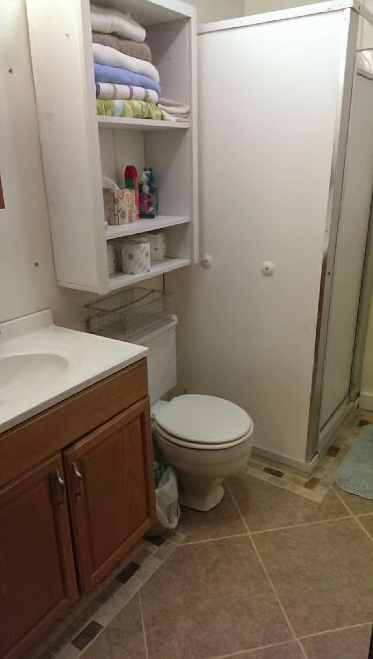 A bathroom with a toilet, a sink, a cabinet, and a shelf with folded towels.