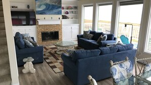 Sala de estar com sofá azul, mesa de centro de vidro e lareira. Estantes com objetos decorativos e um quadro acima da lareira.
