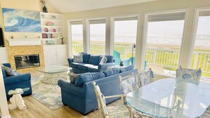 Uma sala de estar com mesa de vidro e mobiliário azul, lareira e vista para a praia.