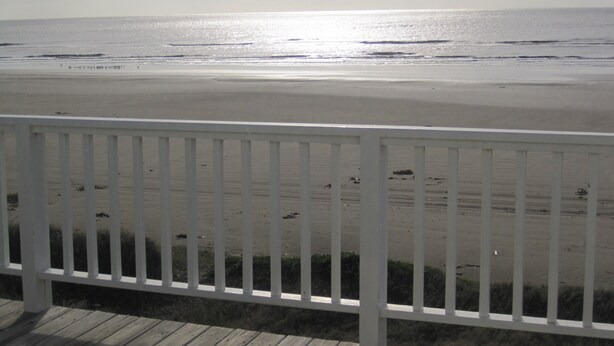 Vista da praia com um deck de madeira e guarda-corpo branco.