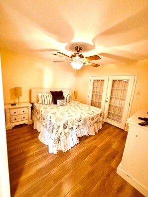 A bedroom with a bed, nightstands, a ceiling fan, and a door with glass panels. - Beachfront/Gulf Front Property/Dog Friendly (Galveston)