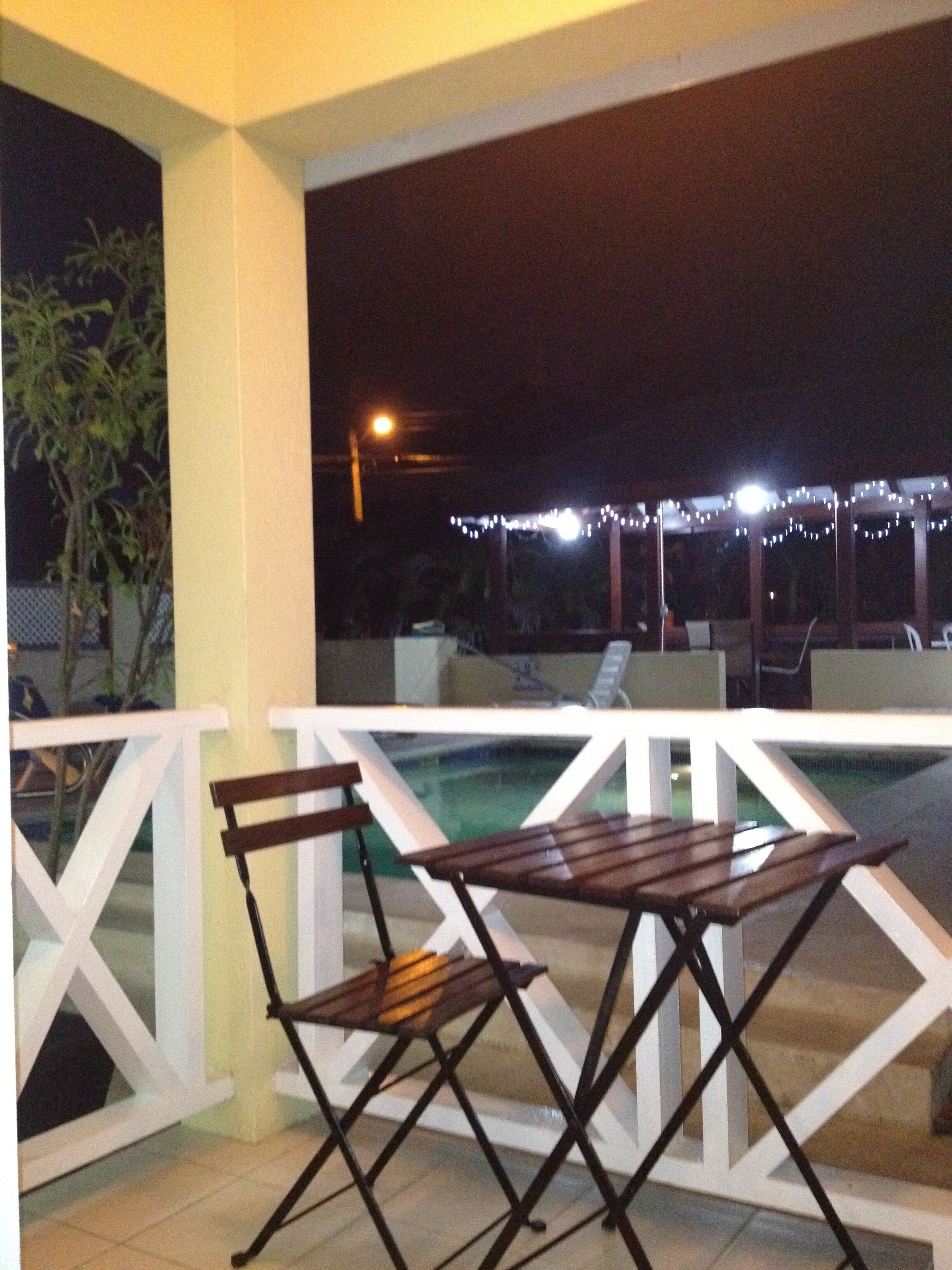 An outdoor seating area with a pool, white railings, and string lights.