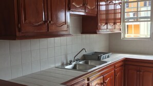 Cocina con armarios de madera, encimera blanca y ventana con vistas a edificios.