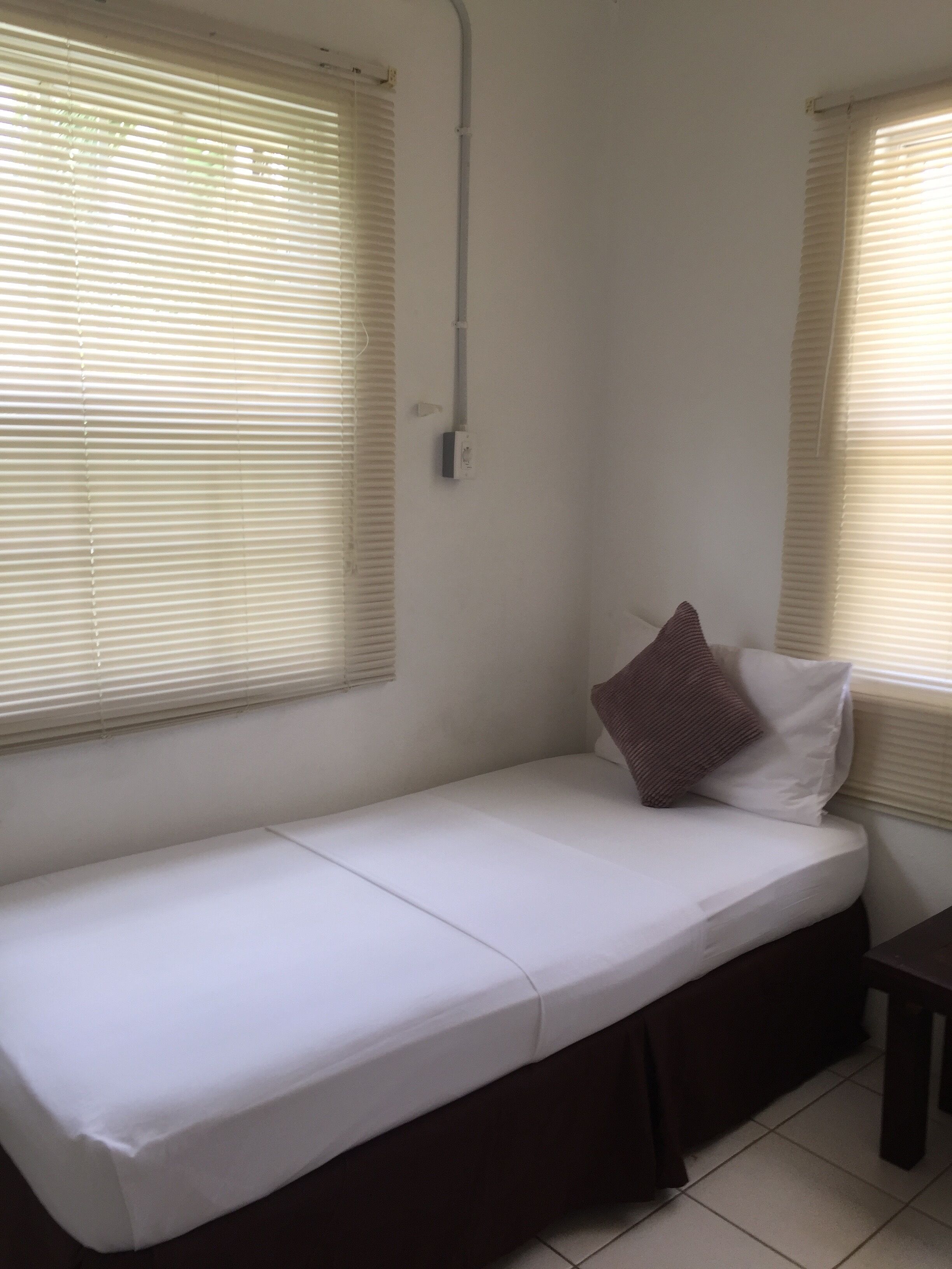 Una habitación pequeña con cama individual, ventana en una pared y toma de corriente en la pared.