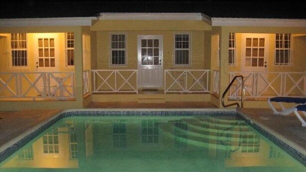 Una piscina con solárium de baldosas, una valla blanca y un edificio con varias ventanas y puertas.