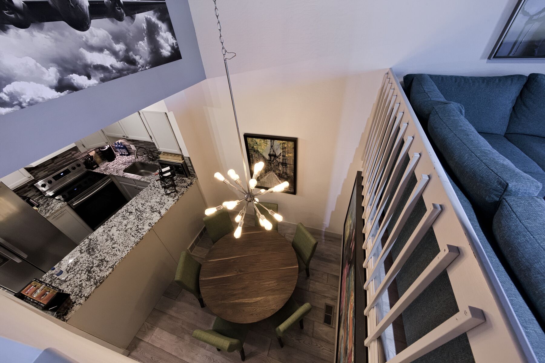 Eine moderne Küche mit Granit-Arbeitsplatte, Edelstahlgeräten und einem Essbereich mit rundem Holztisch und grünen Polsterstühlen.