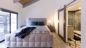 A bedroom with a large bed, a bedside table, a nightstand, a window, and a sliding door leading to a bathroom. - True Ski in Ski Out in Old Town. Newly Renovated. Walk To Main St. (Park City)