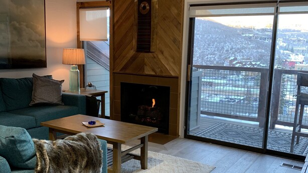 A modern living room with a fireplace, a sofa, a coffee table, and a view of a snowy landscape through a large glass door. - True Ski in Ski Out in Old Town. Newly Renovated. Walk To Main St. (Park City)