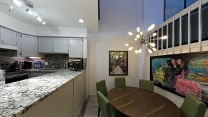 A modern kitchen with granite countertops, white cabinets, and a built-in oven. There is a dining area with a wooden table and green upholstered chairs. - True Ski in Ski Out in Old Town. Newly Renovated. Walk To Main St. (Park City)