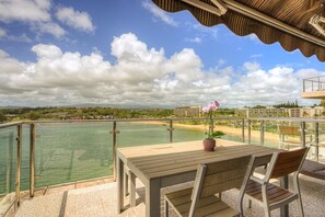 A balcony with a wooden table and chairs overlooking a body of water and a beach. - PRIVATE Ocean Front Cottage Over Looking  Beautiful Kalapaki Bay (Lihue)