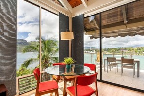 Una camera moderna con un tavolo in vetro e sedie rosse, ampie finestre con vista su un lago e montagne, e un soffitto in legno.