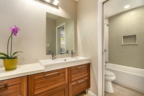 A bathroom with a white sink, wooden cabinets, a mirror, and a bathtub. - PRIVATE Ocean Front Cottage Over Looking  Beautiful Kalapaki Bay (Lihue)