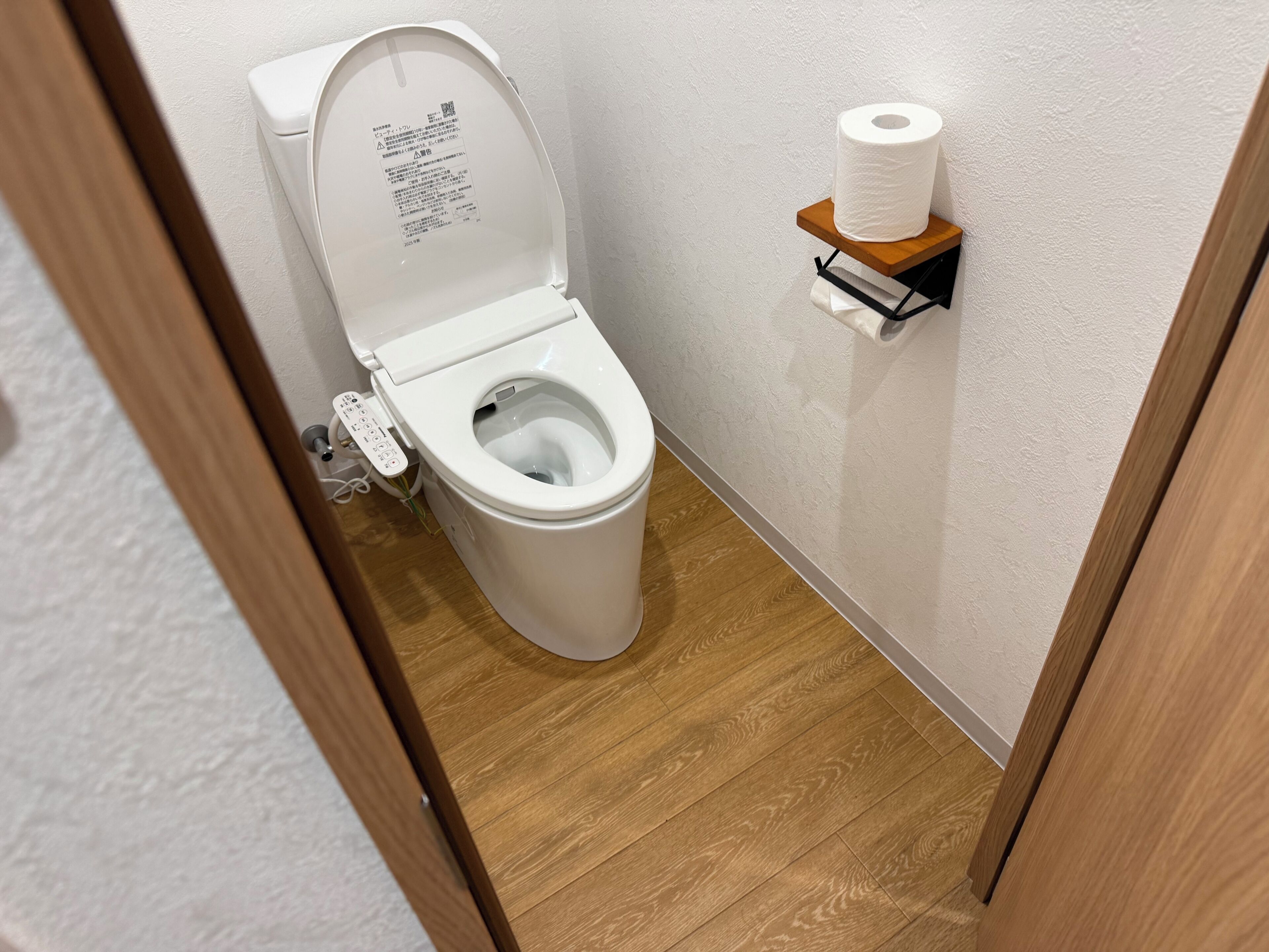 A modern toilet with a control panel, a toilet paper holder on the wall, and a wooden floor.