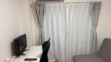 A room with a desk, a chair, a bed, an air conditioner, and a curtain.