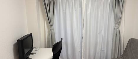 A room with a desk, a chair, a bed, an air conditioner, and a curtain.
