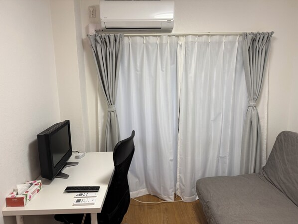 Une pièce comprenant un bureau, une chaise, un lit, un climatiseur et un rideau.