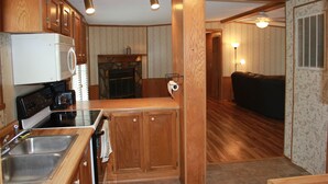 A kitchen with wooden cabinets, a microwave, and a stove. There is a dining area with a couch and a lamp. - Rider's Rest #1: Within 2 Miles Of Tryon International Equestrian Center (Rutherfordton)