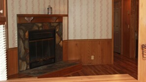 A room with a stone fireplace, wooden paneling, and a door leading to another room. - Rider's Rest #1: Within 2 Miles Of Tryon International Equestrian Center (Rutherfordton)