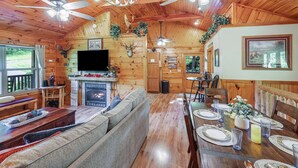 A cozy cabin interior with a wooden dining area, a fireplace, and a television mounted on the wall. - Amazing & beautiful with huge yard for kids to play with outdoor games, fire pit (Sevierville)