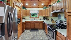 A kitchen with wooden cabinets, a stainless steel refrigerator, a stove, and a window with a view of greenery. - Amazing & beautiful with huge yard for kids to play with outdoor games, fire pit (Sevierville)