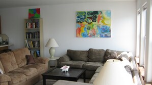 Un salón con un conjunto de sofá, una mesa de centro, una lámpara, una estantería y un cuadro abstracto y colorido en la pared.