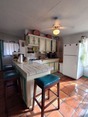 A kitchen with a central island, bar stools, a refrigerator, and a microwave. - Casita Rael, an Art lovers get-a-way (Taos)
