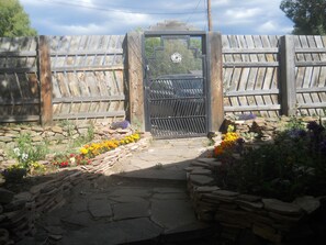 A wooden gate with a metal gate, surrounded by a stone pathway and colorful flowers. - Casita Rael, an Art lovers get-a-way (Taos)